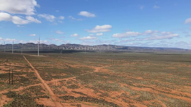 Drone aerial moving backwards in Australian outback desert country road with renewable energy wind farms near mountains