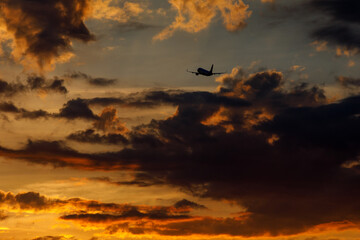Silhouette of an airplane flying at sunset clouds.