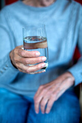 close-up of an older womans hand holding a glass of water