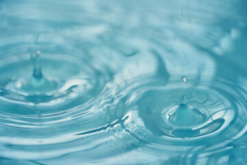 Drop of water drop to the surface. Waves on the surface of the water blue background                              