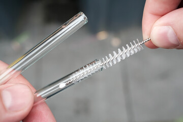 Hands holding reusable glass straws for cocktails and cleaning them with a special brush on a...