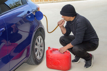 Image of a thief dressed all in black sucking gasoline from a parked car with a rubber hose....