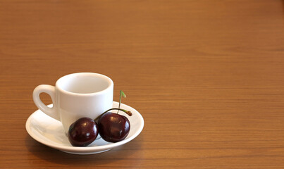 A cup of coffee with two red cherries, on a wooden table