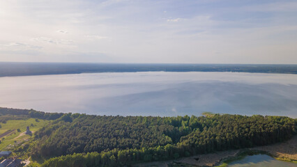 Aerial view of lake and small village on the peninsula. Sunset evening light by calm water on warm beautiful summer day.