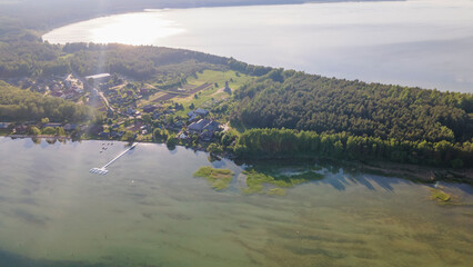 Fototapeta premium Aerial view of lake and small village on the peninsula. Sunset evening light by calm water on warm beautiful summer day.