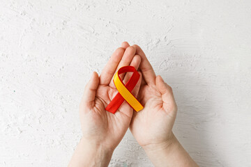 World hepatitis day. Adult hands holding red yellow ribbon on white background. Awareness of prevention and treatment viral hepatitis. Liver cancer. World cancer day.