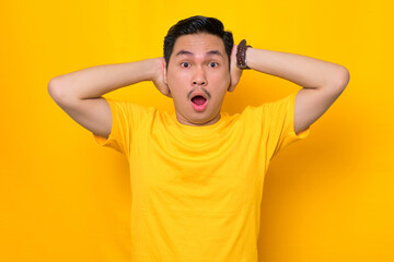 Fototapeta na wymiar Shocked young Asian man in casual t-shirt with open mouth looking at camera in amazement isolated on yellow background. People lifestyle concept
