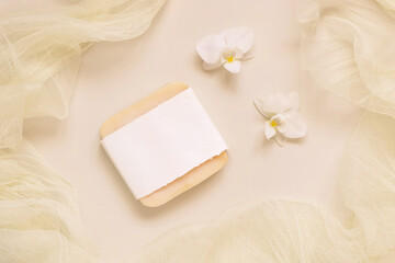 Soap bar near white orchid flowers on light yellow top view. Mockup. Skincare product
