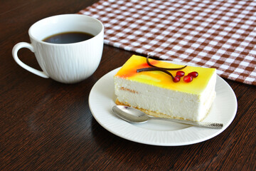 lemon cake with cream on white saucer and cup of coffee on wooden background