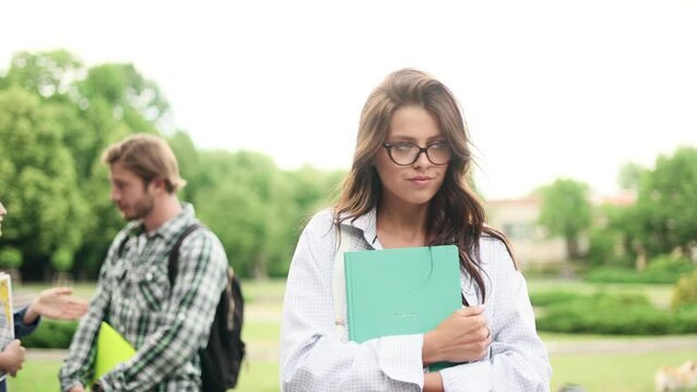 Jealous brunette student girl watching her friend flirting with guy she likes. Unhappy girl in the campus park.