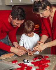 Vertical family photo. Dad, mom, child son boy 4 years bake cookies. Teamwork. Happy family. Christmas baking at home in kitchen, dressed in red color,