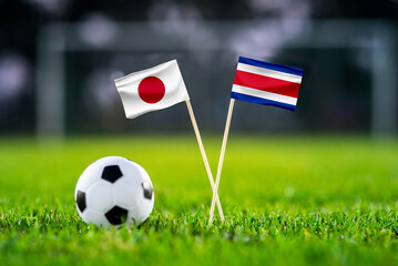October 2022: Japan vs Costa Rica, Ahmed bin Ali Stadium, Football match wallpaper, Handmade national flags and soccer ball on green grass. Football stadium in background. Black edit space.