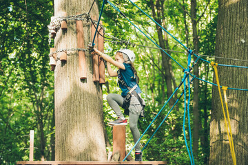 Little girl overcomes the obstacle in the rope park. Child enjoying activity in a climbing adventure park on a summer day. 