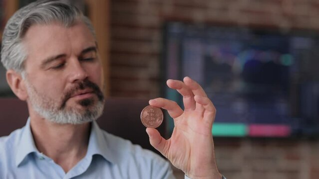Portrait of businessman holding bitkoin in office interior with stock market graphs on background. Using bitcoins as payment. Investitions in cryptocurrency. Buying and selling using bitcoin.