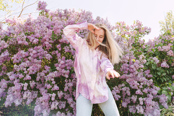 Young blond woman dance emotional among lilac flowers