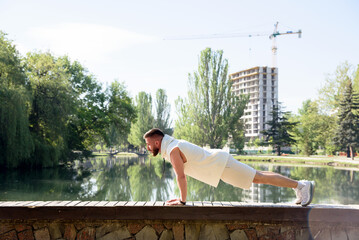 Young brunette man do morning exercises in city park pushing his body up