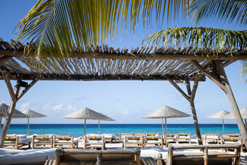 Wooden sun loungers with sun umbrellas on a tropical beach. Beach club.