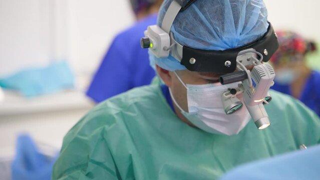 Upper part of a doctor in device glasses on his head. Surgeon looks down and using tools. Close up portrait.