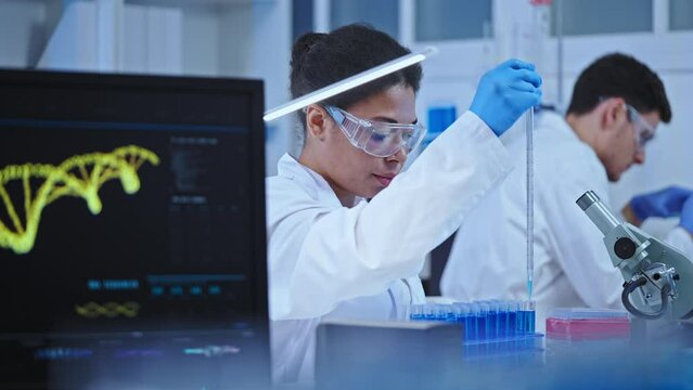 Lab assistant in protective glasses dripping experimental substance in flasks