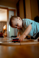 A child playing a toy railway train. The child is sitting on the floor with wooden toys. Toys for a little boy. A preschooler builds a railway and blocks at home, in kindergarten. Educational games fo