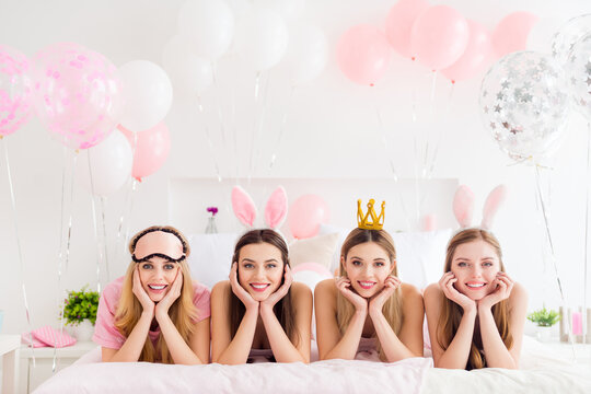 Portrait of four adorable girls hands touch cheeks laying white sheets bed house indoors