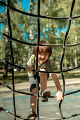 A child climbs up an alpine grid in a park on a playground on a hot summer day. children's playground in a public park, entertainment and recreation for children, mountaineering training.