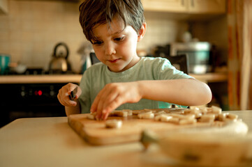 a five-year-old boy helps moms in the kitchen, he cuts a banana for a vegetable salad. The concept of family
