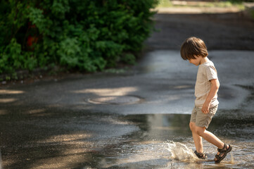 a cute three-year-old Asian boy with long black hair happily stomps through puddles. Happy children...