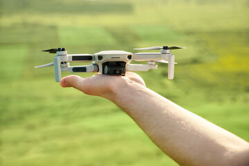 Man's hand is holding a drone on a green agricultural field background. Using technology for remote observation and filming of grows plants