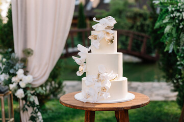 Front close up view of beautiful minimalist wedding cake in white color cream decorated with rose petals decor. Wedding concept. 
