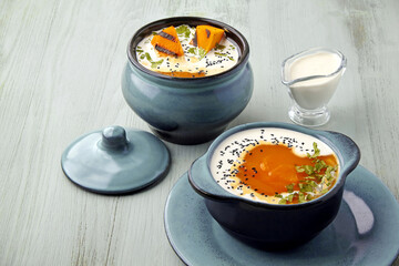 Pumpkin autumn gazpacho puree soup in a pot and bowl with grilled slices and milk