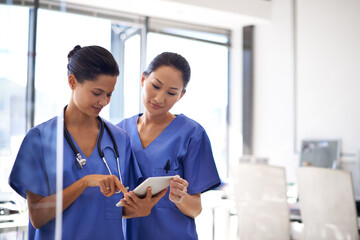 Reviewing patient data. Shot of two female nurses using a tablet to review medical records.