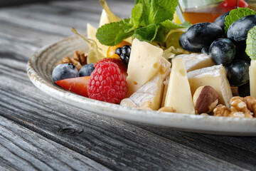 Cheese platter: variety of cheeses on wooden plate with fruits, nuts and berries.