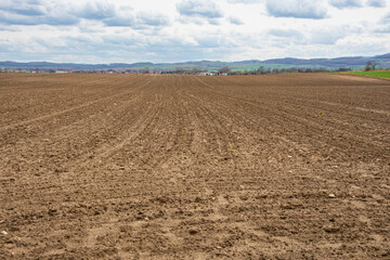 agricultural landscape, plowed field, hills in the background, clouds in the sky