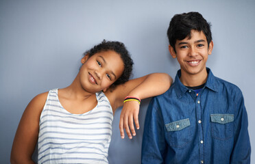 She can always lean on her big brother. A cute brother and sister standing isolated on grey.