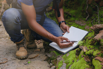 Crop image of Biologist or botanist recording information about small tropical plants in forest....