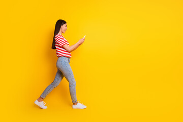 Fototapeta na wymiar Full body profile photo of amazed excited girl walking use telephone typing isolated on yellow color background