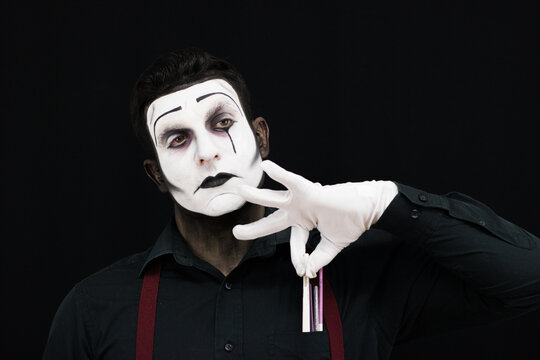 Mime taking a brush from a pocket to start his performance in a black background 