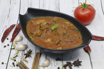 Beef kerala curry traditional Indian spicy chili lamb meat food with rice garnish and tomatoes in black bowl on vintage wooden table background. India culture restaurant dish
