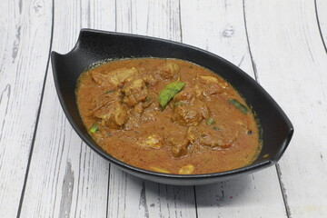 Beef kerala curry traditional Indian spicy chili lamb meat food with rice garnish and tomatoes in black bowl on vintage wooden table background. India culture restaurant dish