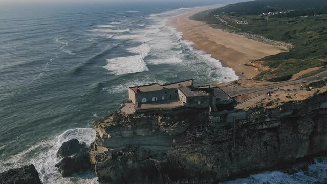 Full circle drone spin around lighthouse on a cliff in Nazare Portugal with Praia do Norte known for biggest waves in the world in the background.