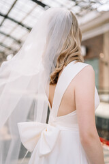 Young woman, blonde bride in a wedding vintage dress with a big bow shot from behind