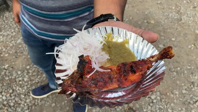 Closeup shot of a man holding Tandoori chicken or Tangri Kabab in silver plate with green chutney and onion in road side Dhaba in India.