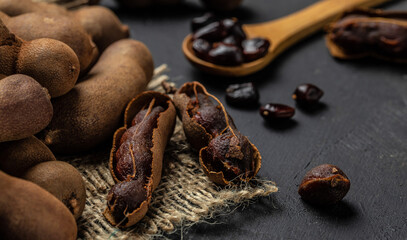 Tropical fruits, Tamarindo beans in shell on a brown butchers block on a dark background, healthy fruit. banner, menu, recipe place for text, top view
