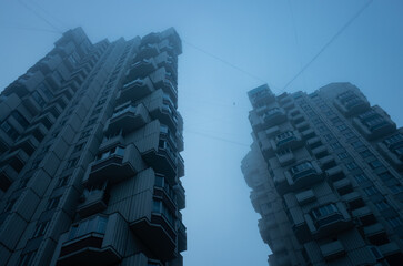 Two tall residential buildings immersed in misty sky. Cyberpunk stylistics.