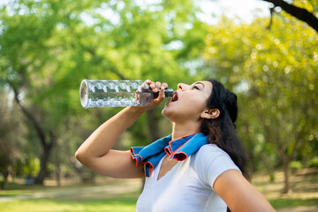 Young tired thirsty indian woman athlete takes a break drinking water with bottle, Asian female out...