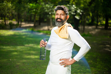 Happy indian beard man athlete takes a break holding water bottle, Asian male standing on a hot day...