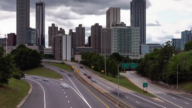 Panning out timelapse of downtown Atlanta from Jackson Street bridge overlooking the highway with motion blur on the vehicular traffic traveling on the roadway below and heavy cloud cover above.