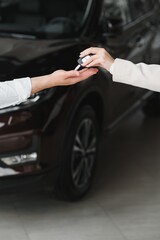 Car sale. Dealer giving key to new owner in auto show or salon, closeup