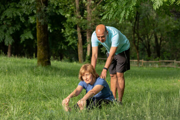 Naklejka na ściany i meble Senior couple, man helping woman gain flexibility while relaxing on the grass in nature enviroment